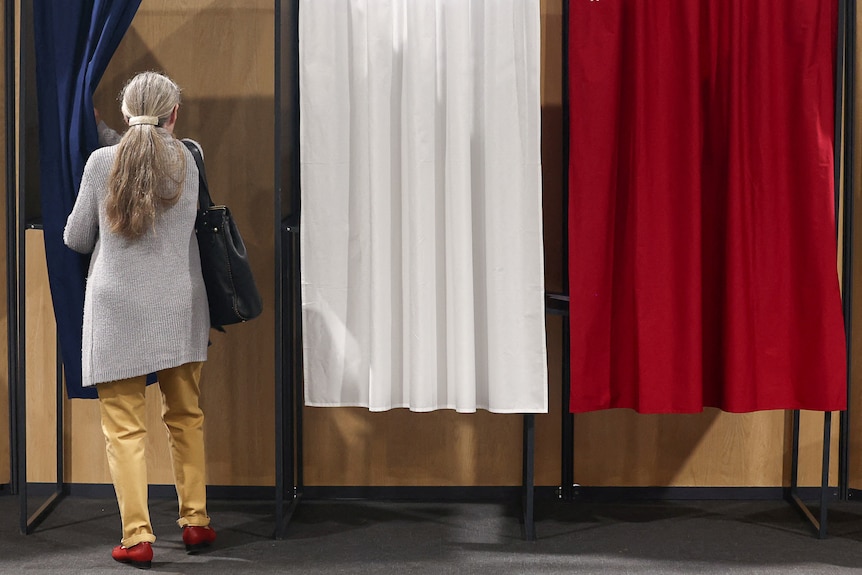 A woman entering a red, white and blue voting booth 