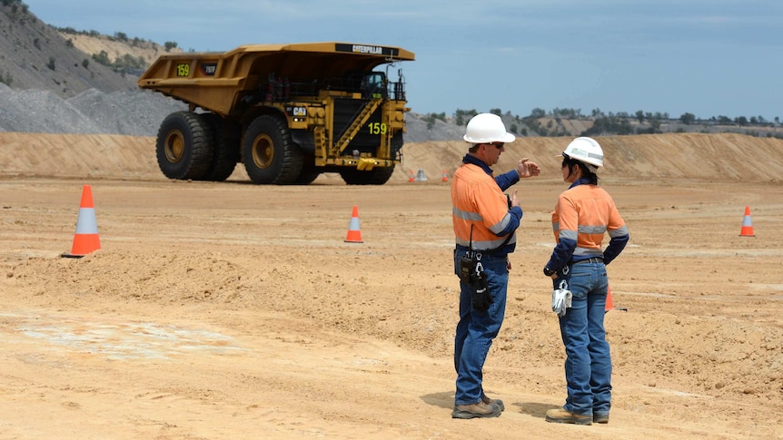 Workers stand at a mine site with trucks in central Queensland
