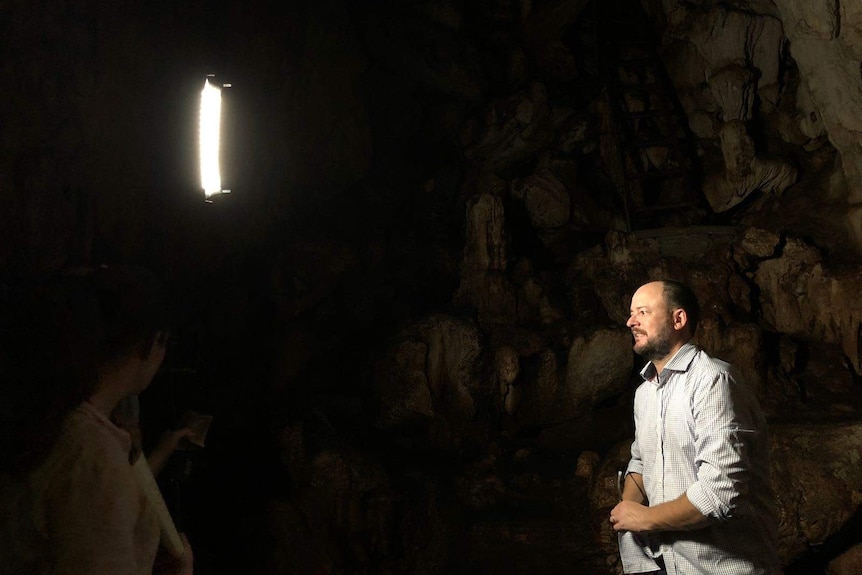 Willacy and crew in dark cave with light on a stand.