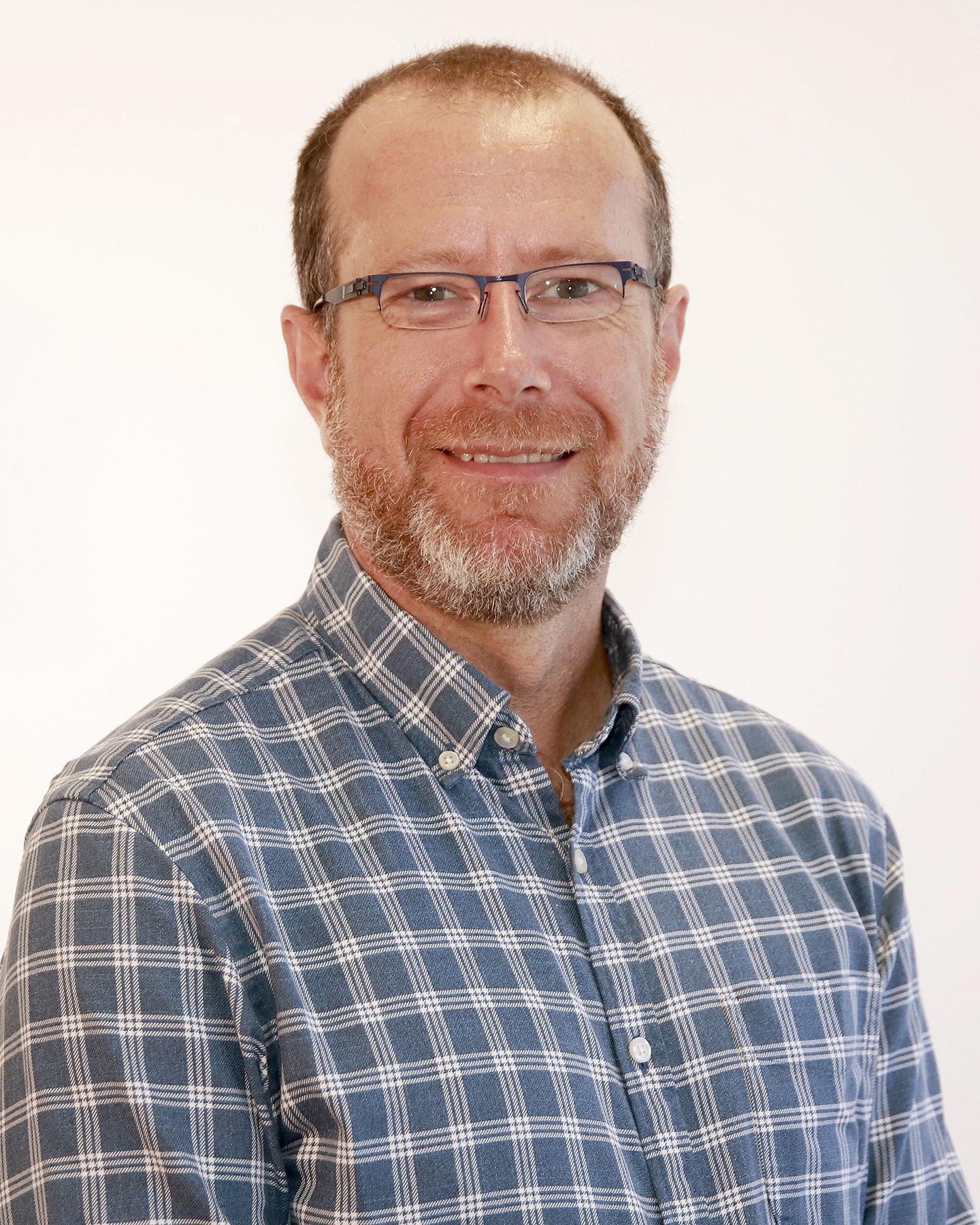 man with beard and glasses in checked shirt smiling at camera