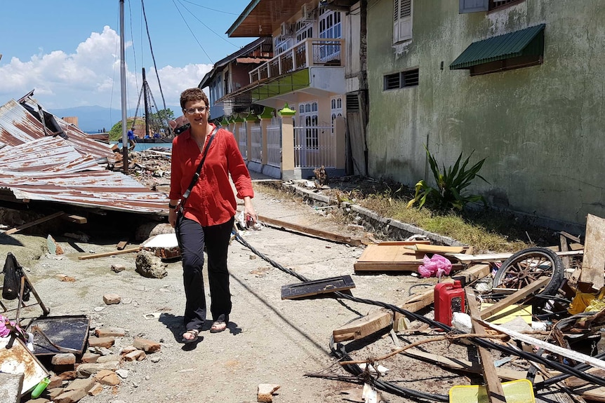 Anne Barker walking amid rubble and damaged buildings.