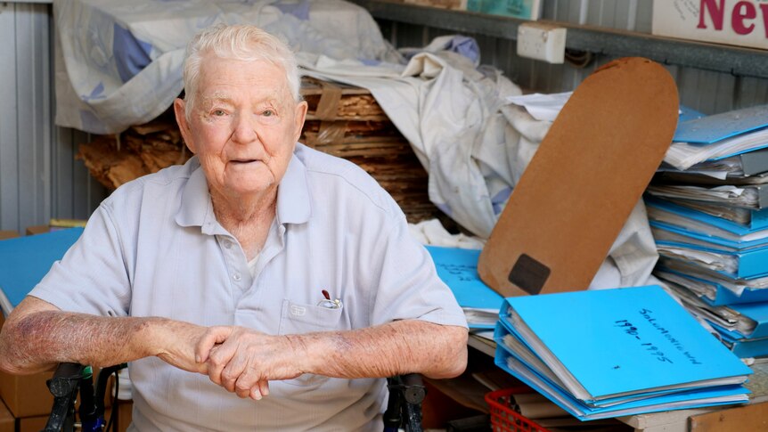 a man sits in front of folders of papers on his walking frame