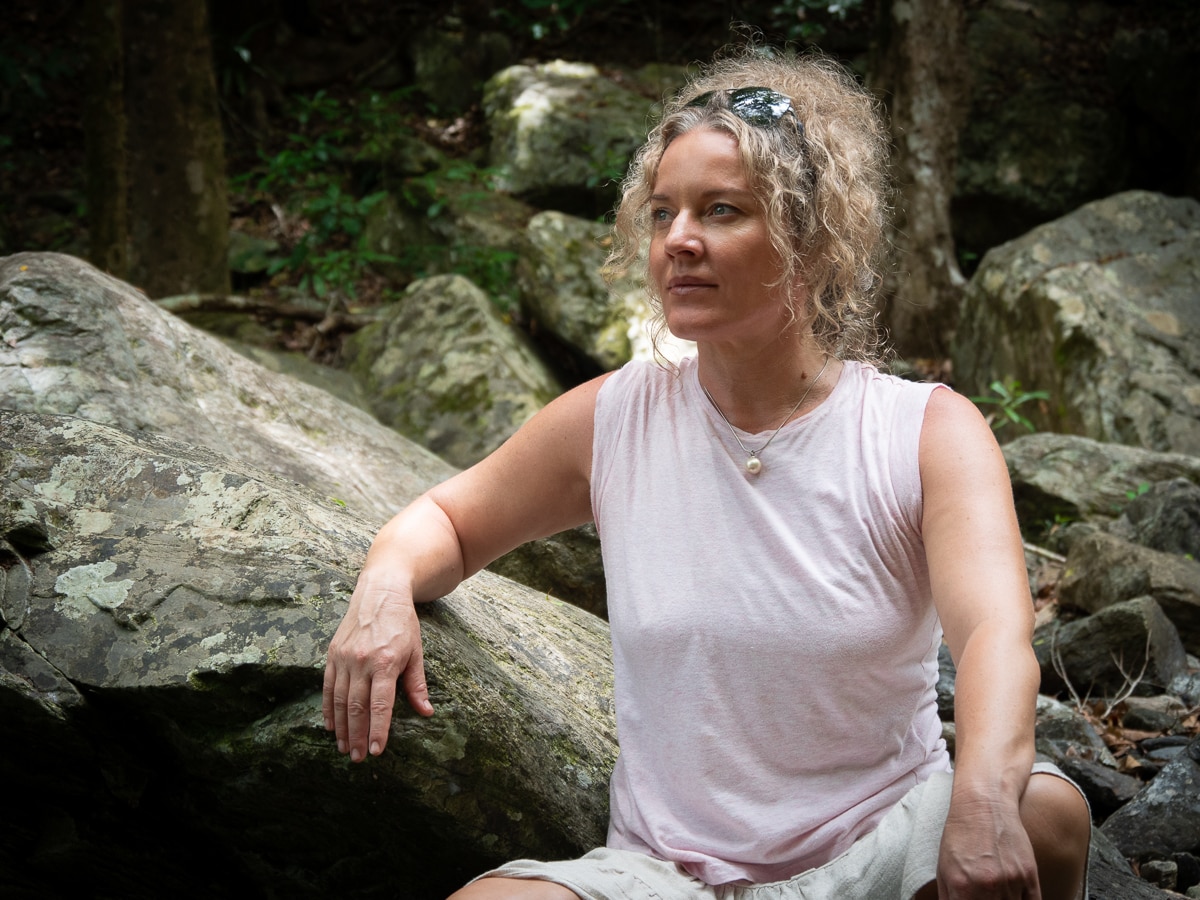 Sarah Rees leaning against a rock, looking thoughtfully into the distance.