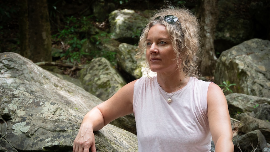 Sarah Rees leaning against a rock, looking thoughtfully into the distance.