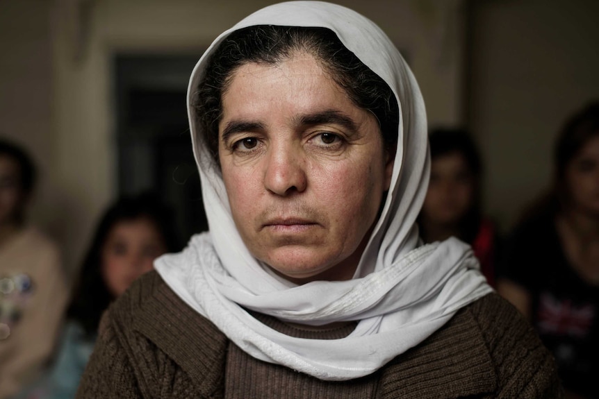 A woman wearing a white head scarf looks directly at the camera.