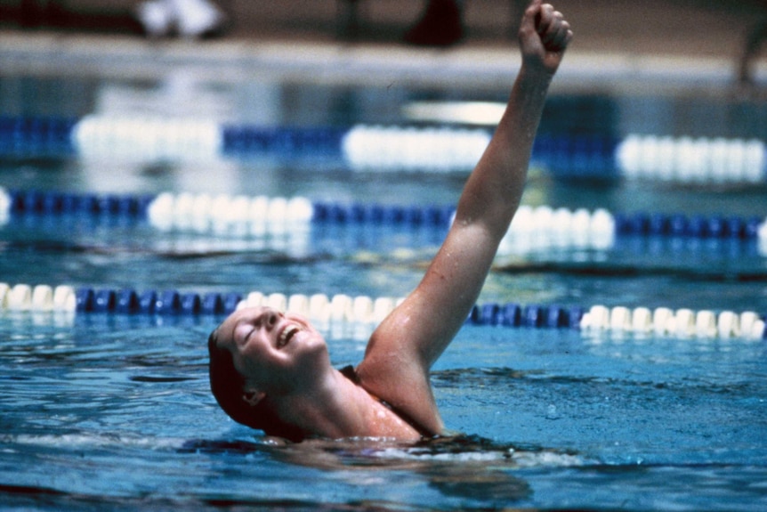 A swimmer holds her arms up in triumph and relief after a race