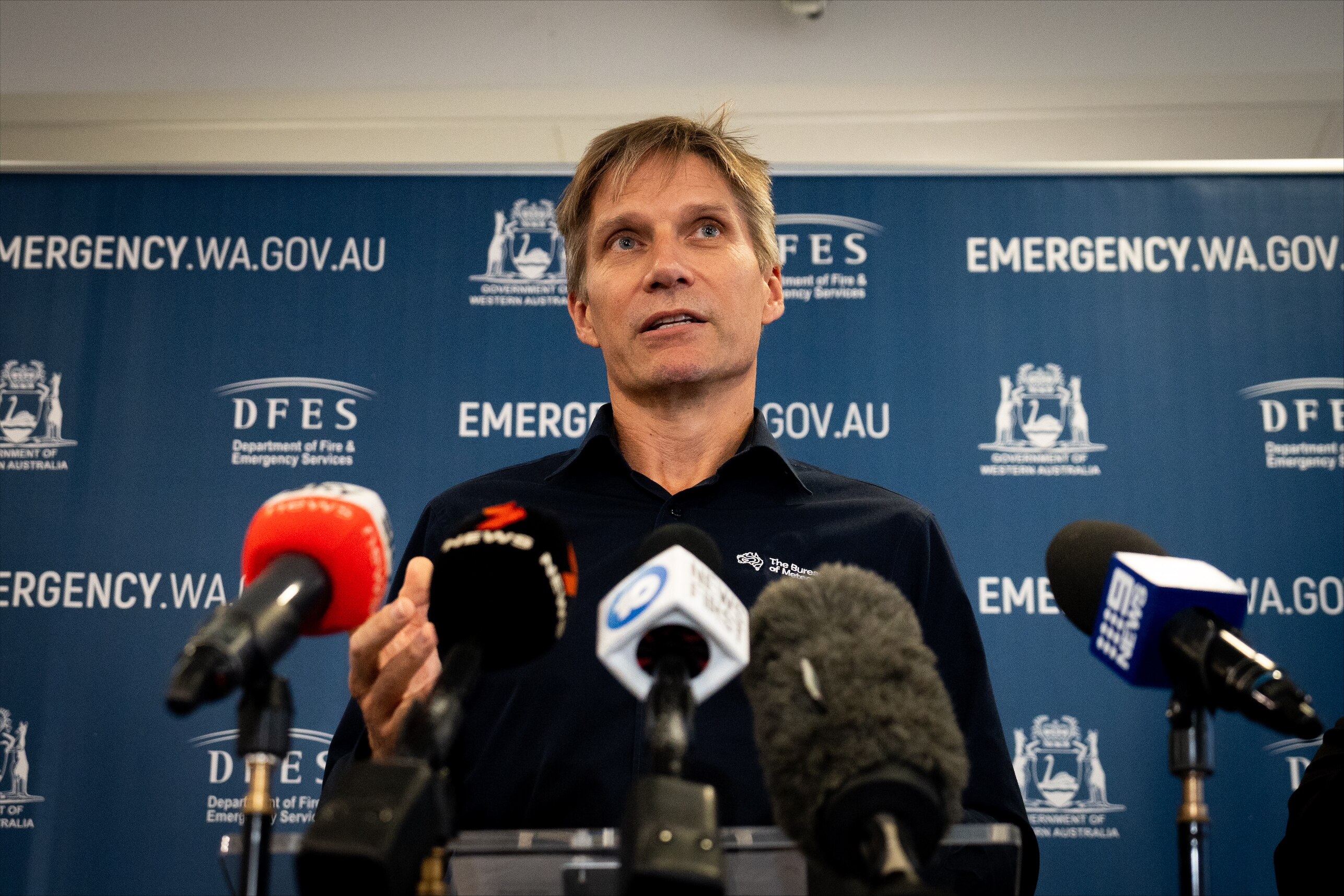 A man in a black shirt stands at a lectern.