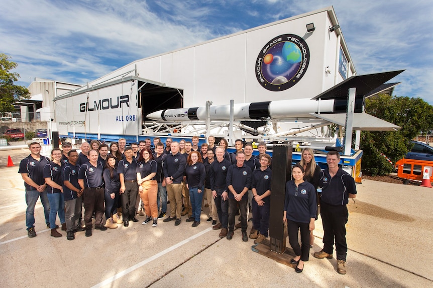 A group of people standing in front of a rocket.