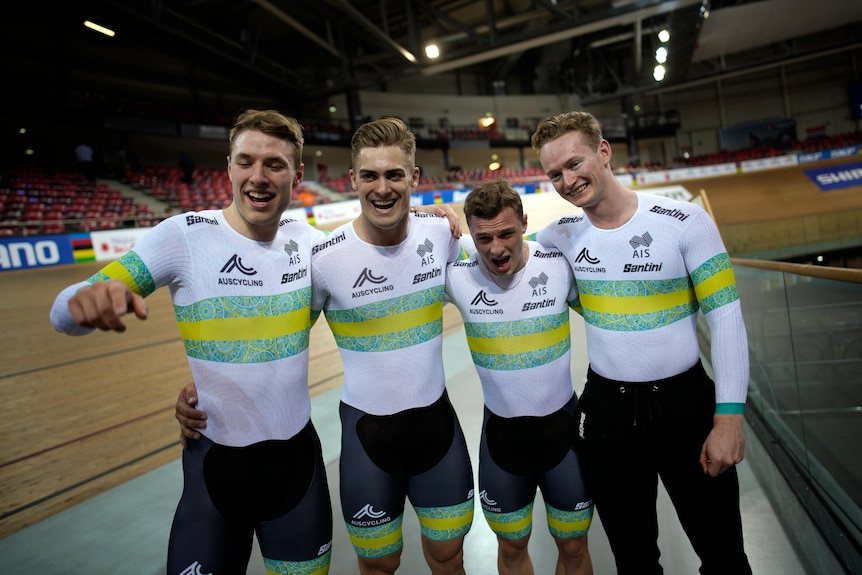 Four Australian cyclists smile and laugh at the camera as they stand on the track after winning a gold medal.