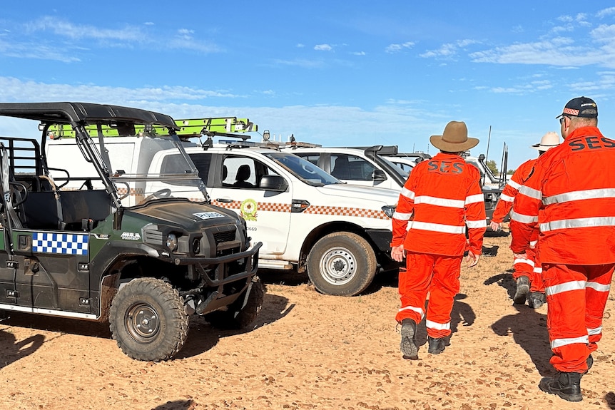 men in SES uniforms walk past an all terrain vehicle and four wheel drives
