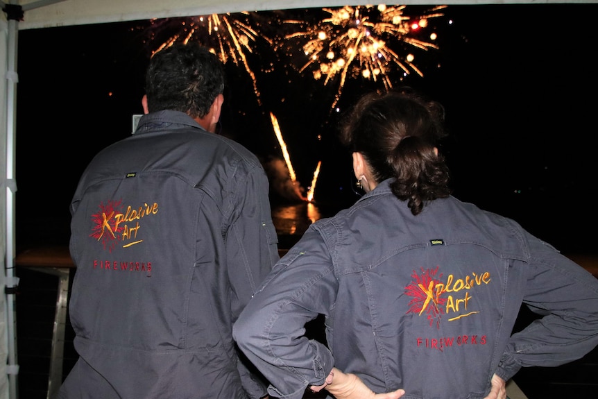 Mike and Karen have their back to the camera as they look on at fireworks shooting off in the distance, 