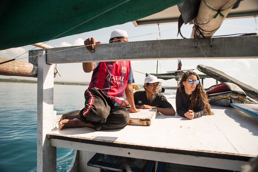 Two men and a woman relax at the bow of a fishing boat