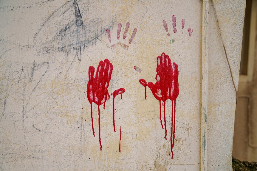 A pair of red hand prints are seen on a dirty external wall