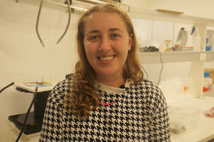 Young woman Vanessa Clark stands in a laboratory and smiles at camera