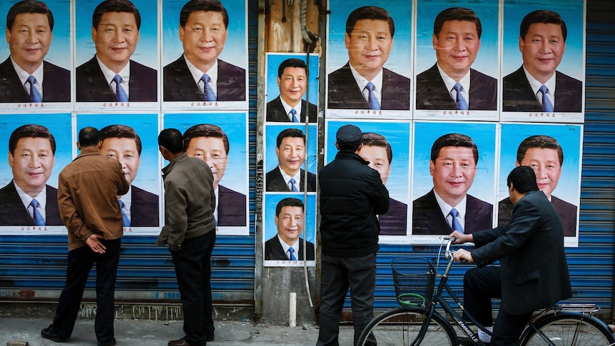 People look at a building covered in posters of Chinese President Xi Jinping.