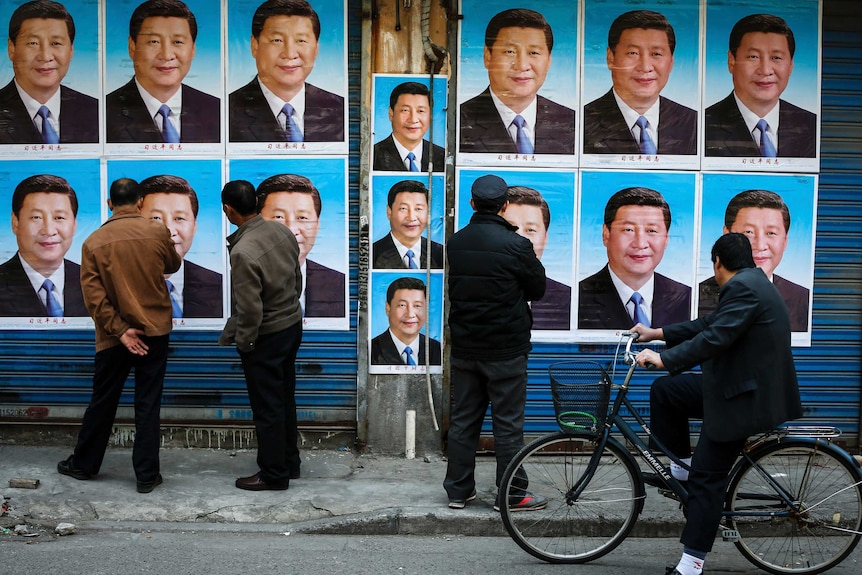 People look at a building covered in posters of Chinese President Xi Jinping.