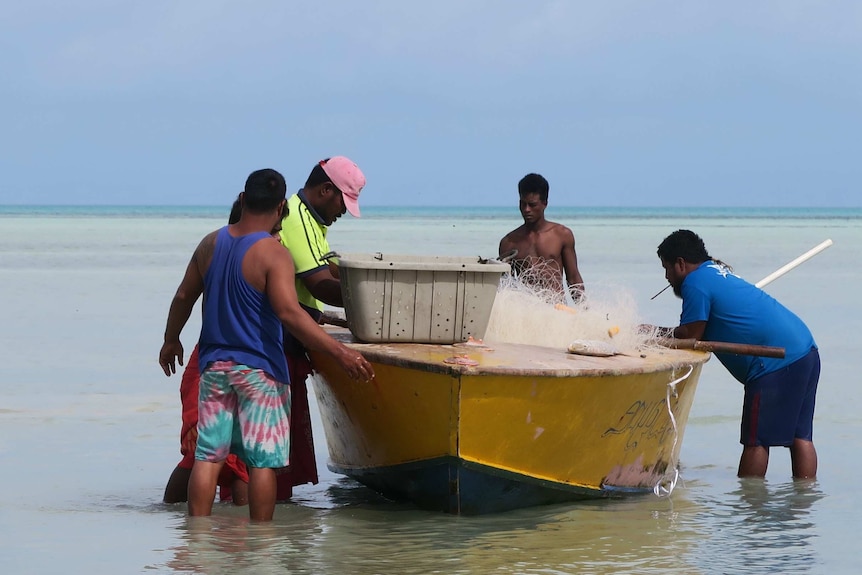 Fishermen crowd around a boat on a lagoon