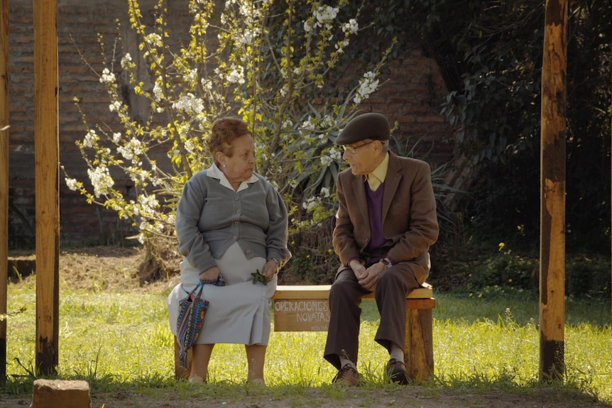 An elderly man, the spy Sergio Chamy, sitting outside next to an elderly woman in a garden in documentary The Mole Agent