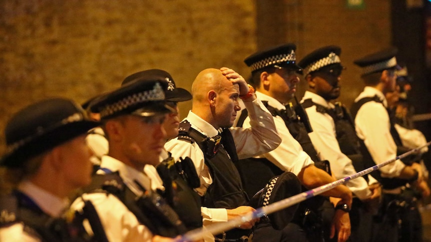 An officer takes off his hat and looks distressed as officers line up near a police cordon in Finsbury Park.