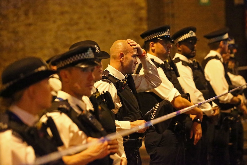 An officer takes off his hat and looks distressed as officers line up near a police cordon in Finsbury Park.