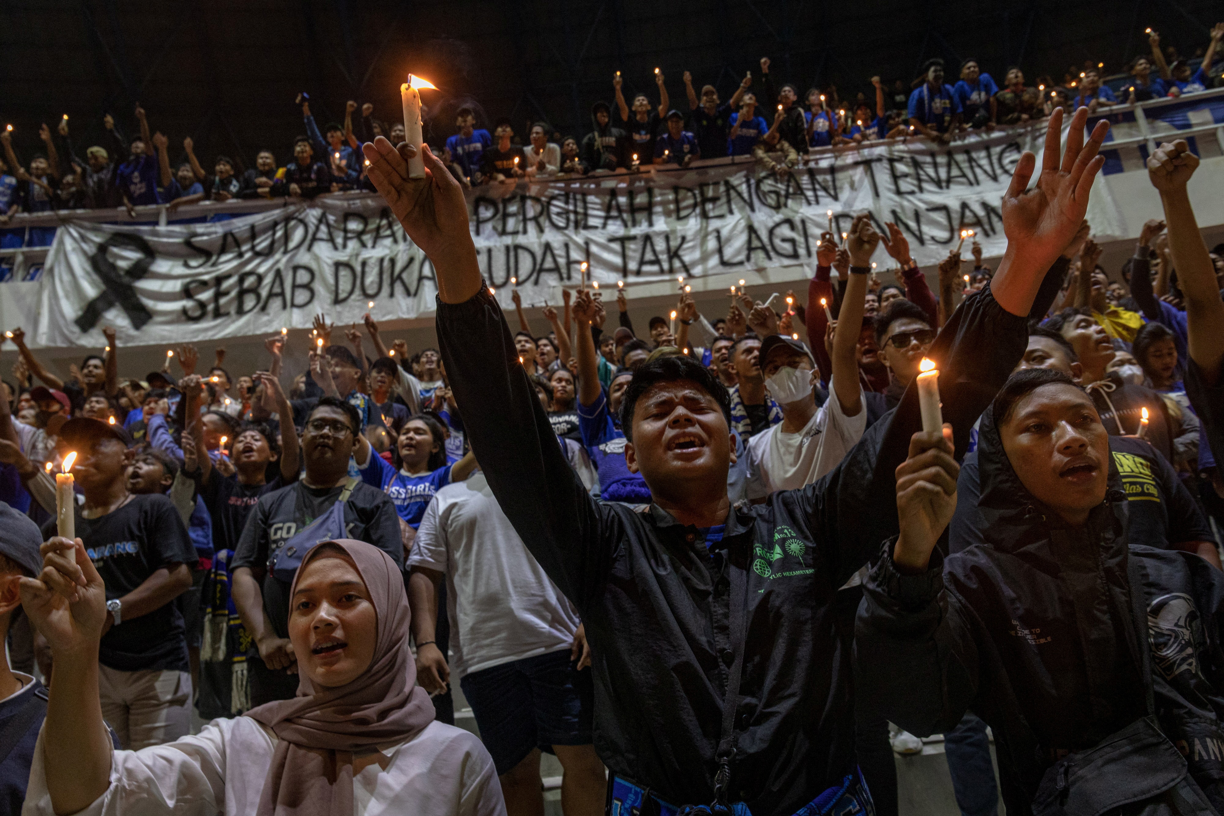 Hundreds of people hold candles at a football stadium as part of an evening vigil.
