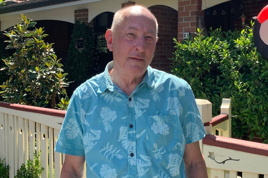 A man in a blue shirt standing in front of his house.