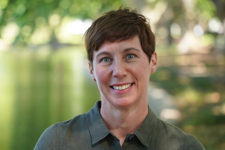 A woman with short hair and a green dress poses for a photo at a lake