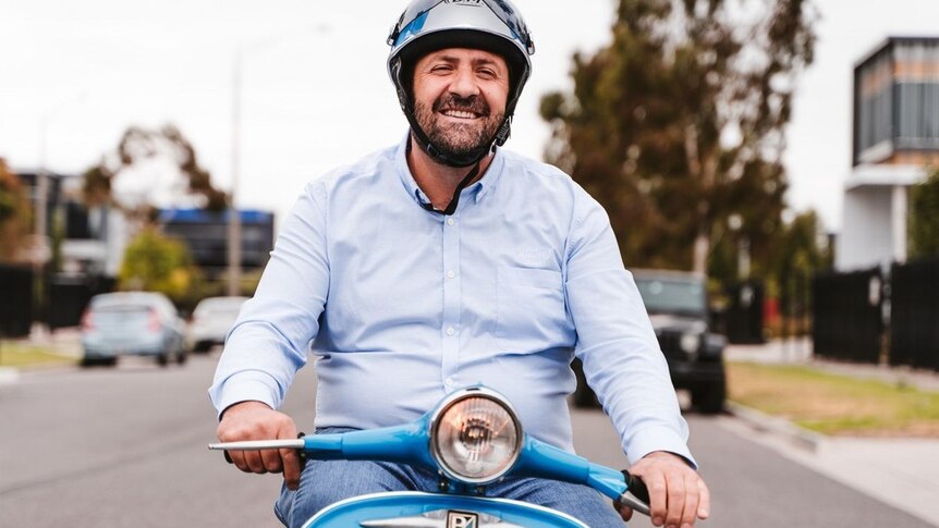 Man riding blue Vespa, smiling.
