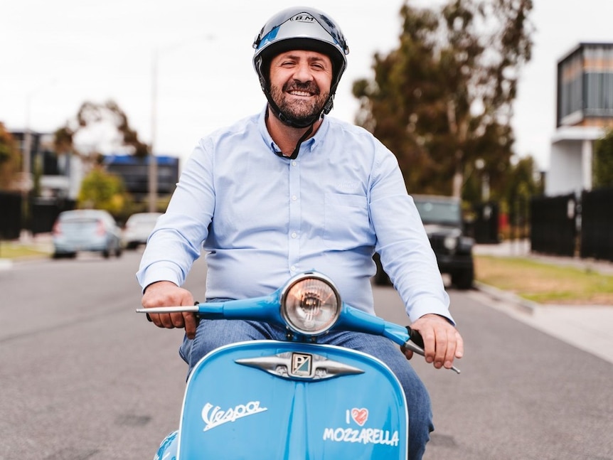 Man riding blue Vespa, smiling.