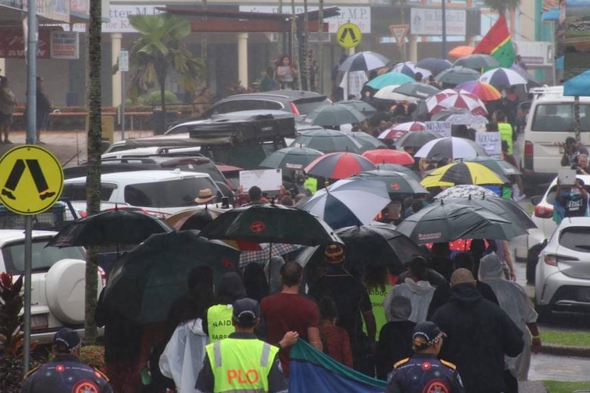 A group of umbrellas cover a crowd of people walking down a main street in the rain.