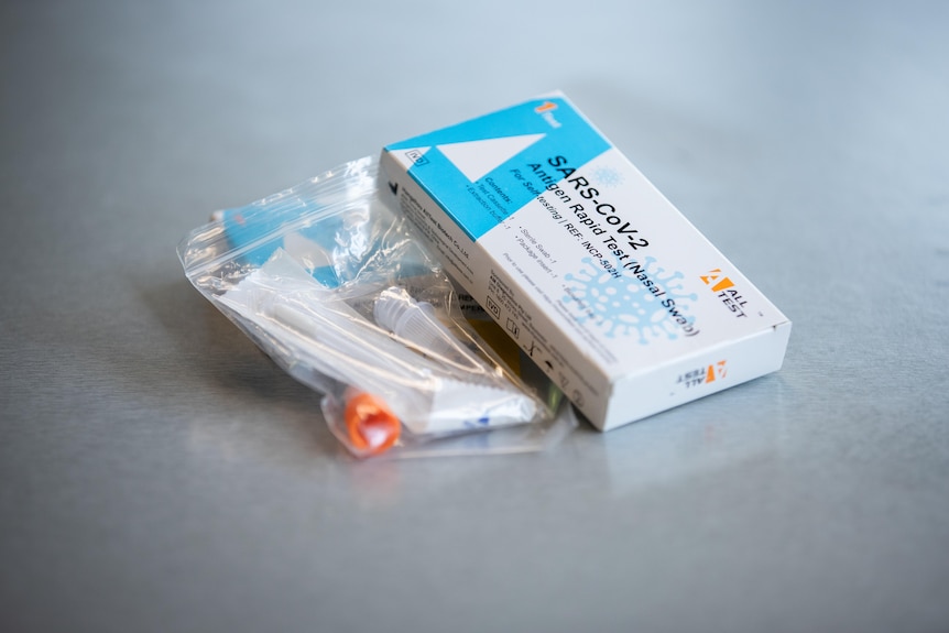 A rapid antigen test in a sealed ziplock back lying next to two boxes of rapid antigen tests.