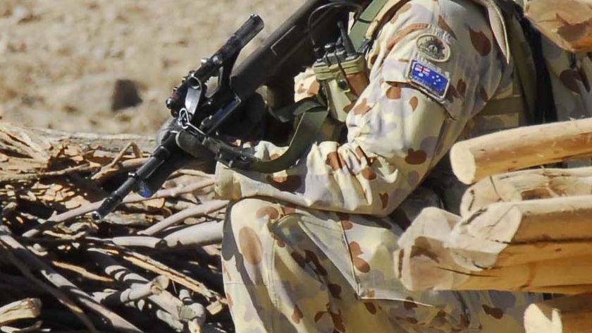 Defence Force soldier kneeling amongst logs