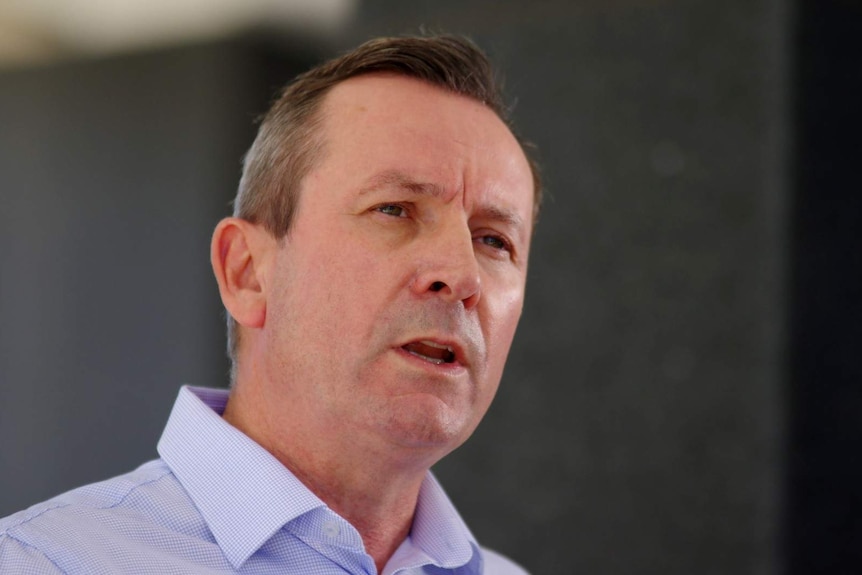 WA Premier Mark McGowan in a blue shirt against a dark grey background talking as es briefs reporters on coronavirus measures.