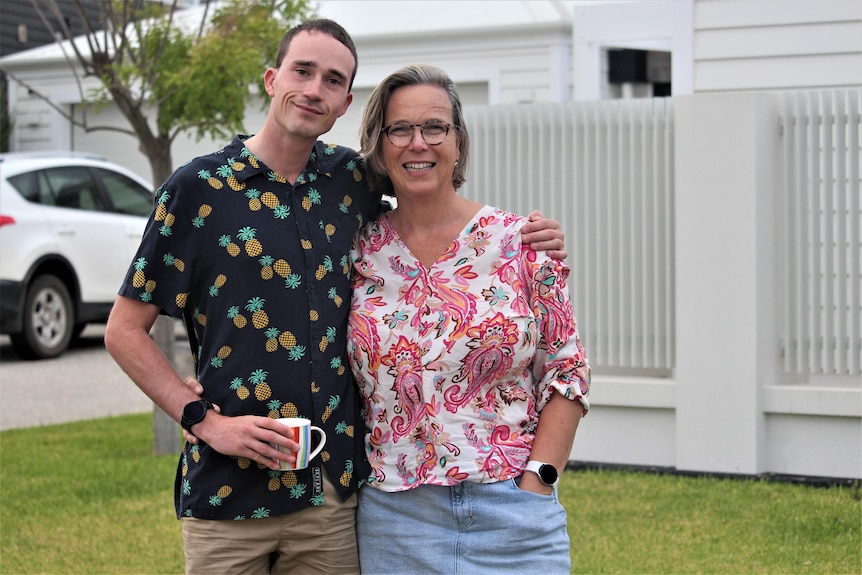 They have their arms around each other, both wear bright shirts, he holds a cup