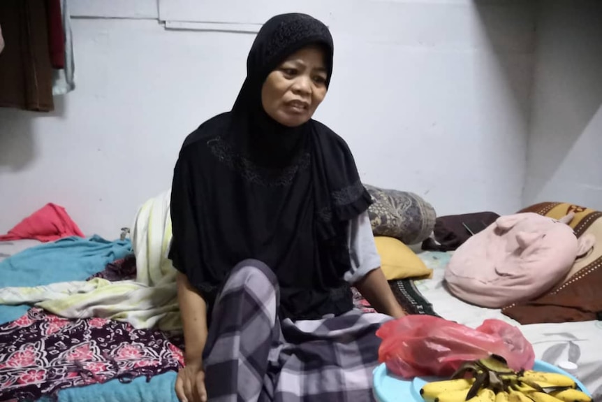 A woman in a black hijab sits on her bed.