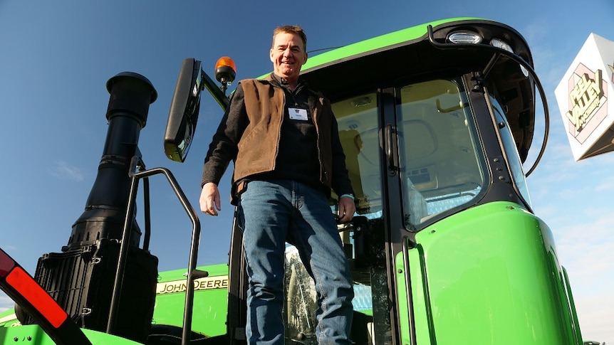 Steve John stands on the steps of a green tractor.