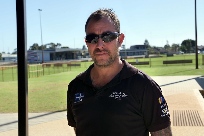 A man wears sunglasses with a grassed area in the background.