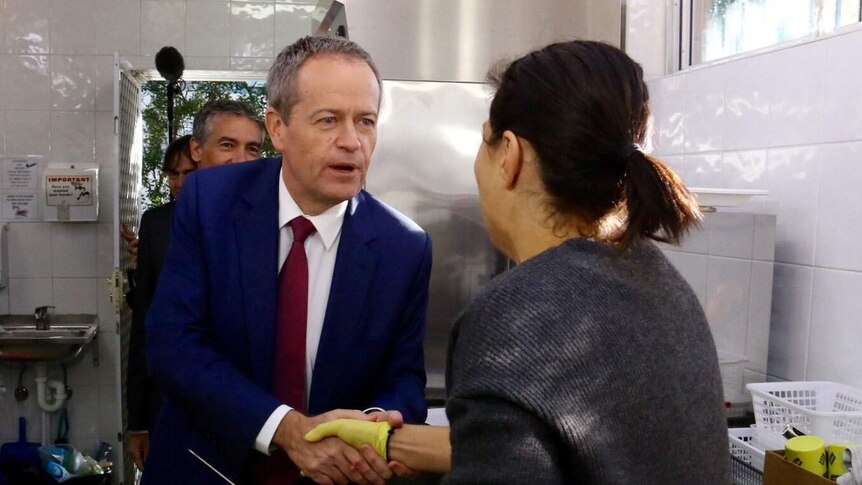 Bill Shorten shakes hands with women in a kitchen who holds a knife