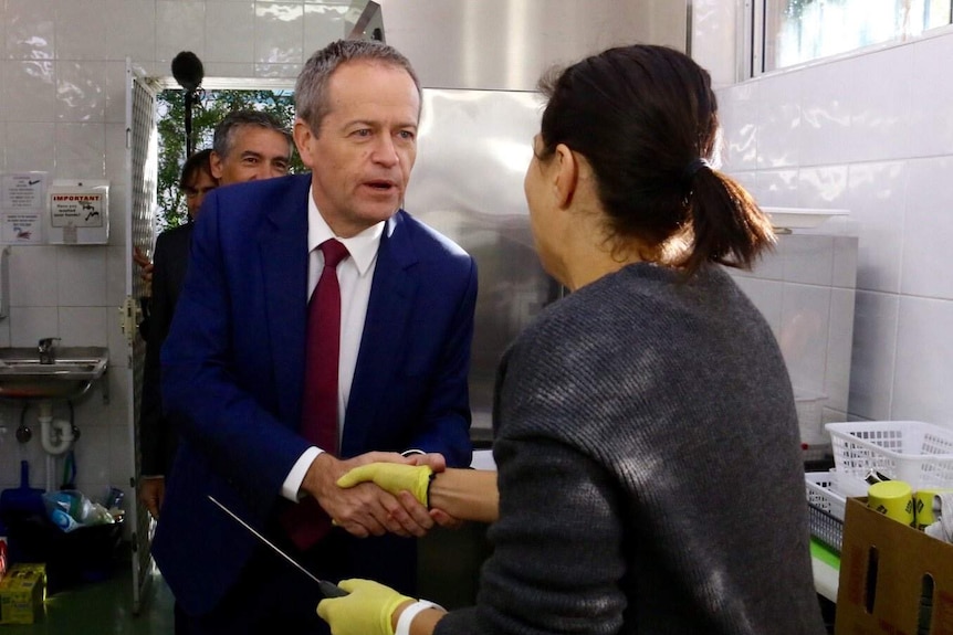 Bill Shorten shakes hands with women in a kitchen who holds a knife