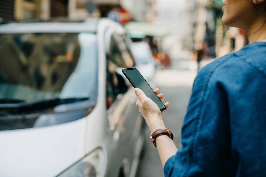 A woman looks up from her phone as cars pass on a busy street.