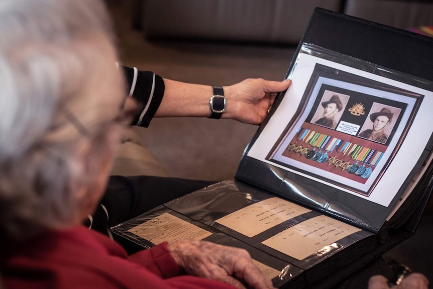 Marie Murray looks at a photo album that shows service photos and medals of her brothers.
