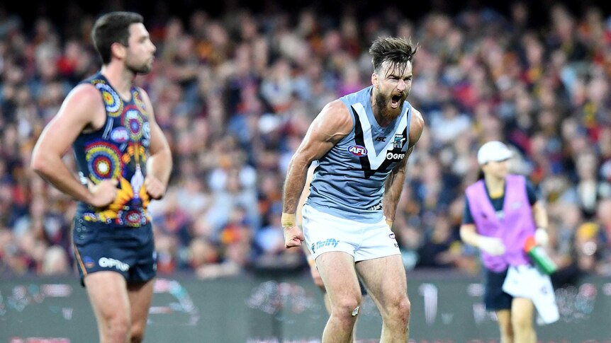 A male AFL player screams out as he hunches his upper body in celebration after kicking a goal.