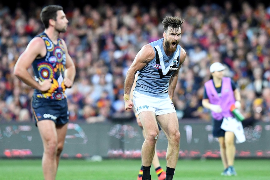 A male AFL player screams out as he hunches his upper body in celebration after kicking a goal.