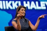 A woman in a blue dress points in front of a sign that reads "Nikki Haley"
