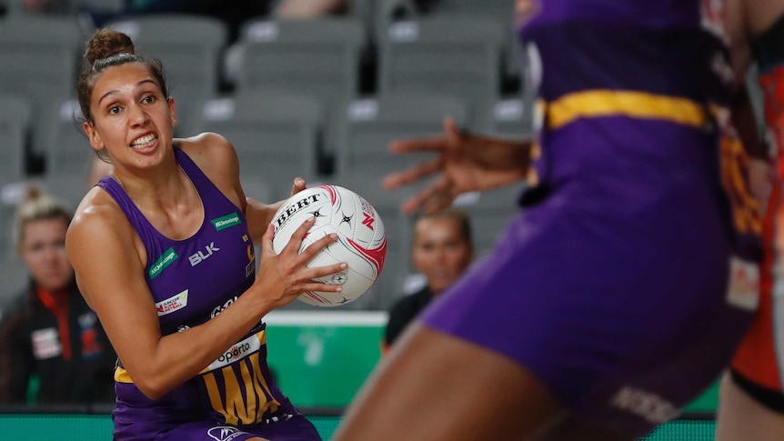 A young woman with dark hair in a purple Firebirds uniform dodges an opponent on the netball court.