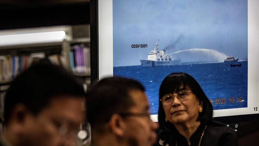Footage of a ship using a water cannon against another vessel is shown during a press conference.