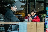 Outside a cafe looking through the window at a man and his son and other patrons