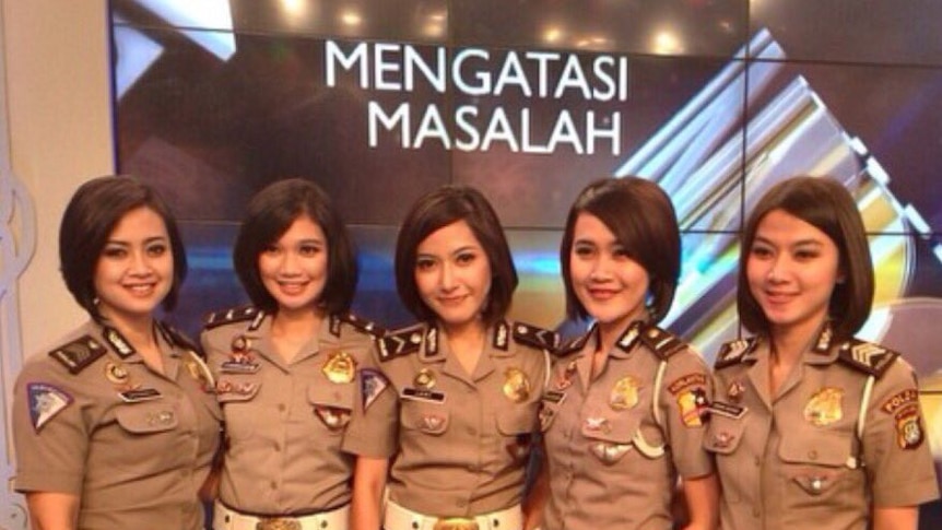 Five policewomen of similar height stand in front of a screen wearing uniform