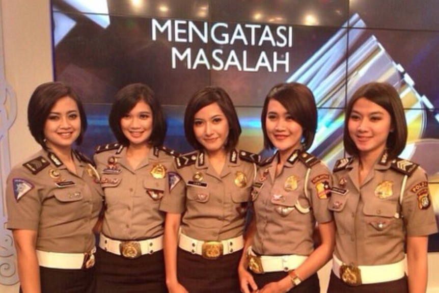 Five policewomen of similar height stand in front of a screen wearing uniform