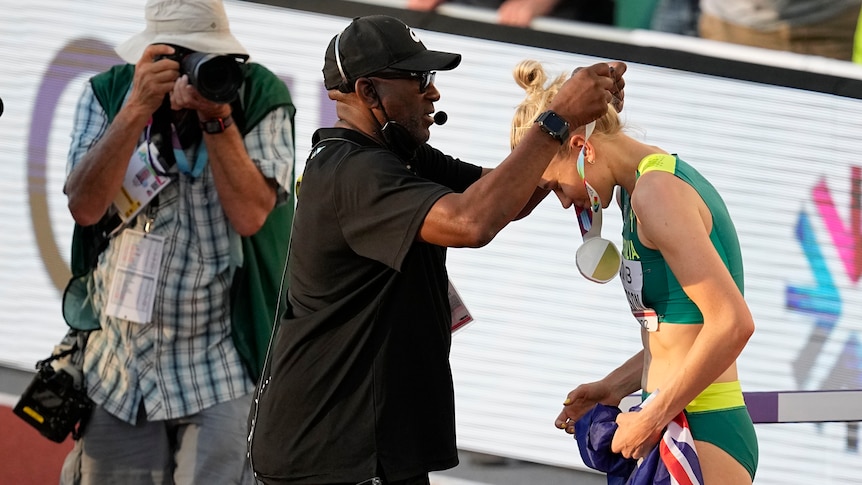 A man in a cap puts a medal around the next of a female athlete